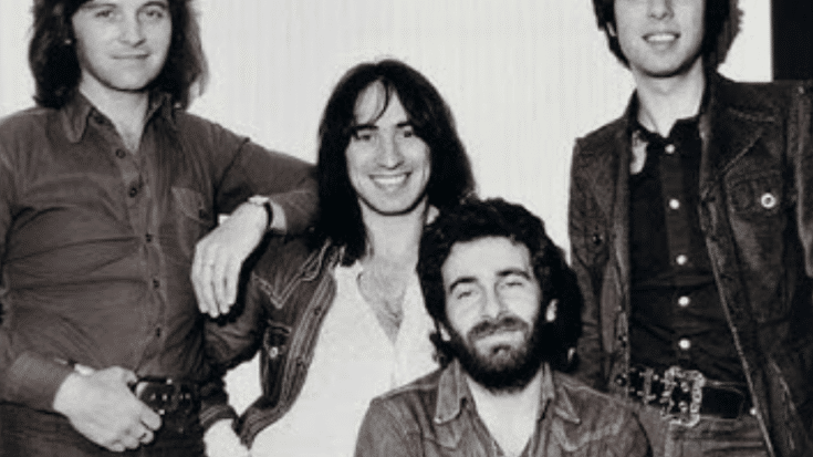 Four members of 10cc pose together in casual denim outfits, smiling and leaning on each other. One member sits in front while the others stand behind him, creating a relaxed and friendly atmosphere.