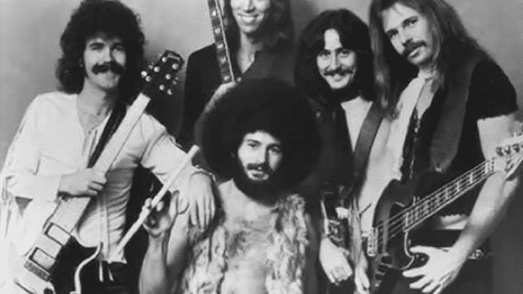 The Doobie Brothers posing together in a classic black-and-white promotional shot, featuring their signature 1970s style with guitars, long hair, and a mix of casual and bohemian clothing.