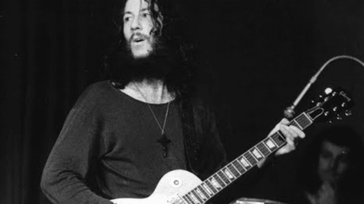 Black-and-white photo of Peter Green, Fleetwood Mac’s founding guitarist, performing onstage with a Gibson Les Paul and wearing a cross necklace.