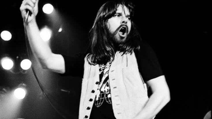 Bob Seger passionately performing on stage with long hair flowing, wearing a vest and gripping the mic mid-verse under bright concert lights