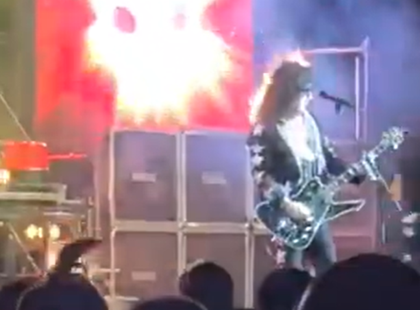 Member of a Kiss tribute band on stage mid-performance with hair briefly catching fire from pyrotechnics