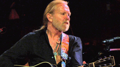 Gregg Allman performing on stage with a guitar during a live concert
