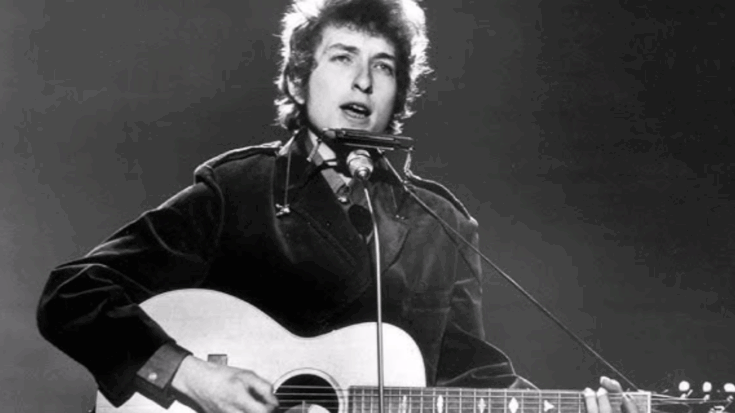 Bob Dylan performing live with acoustic guitar and harmonica during an early folk music concert