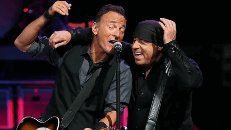 Bruce Springsteen and Steven Van Zandt performing on stage together, smiling as they share a microphone during a live show.