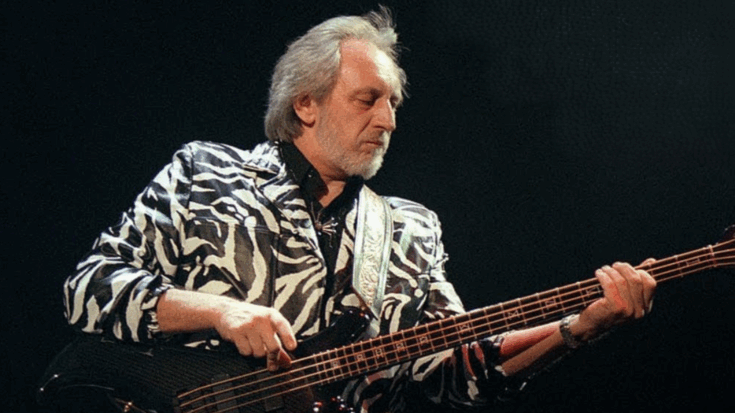 John Entwistle of The Who plays bass guitar on stage wearing a black and white zebra-striped jacket, focused on his instrument under concert lighting.