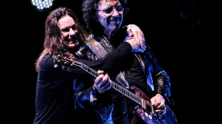 Ozzy Osbourne smiling and embracing guitarist Tony Iommi during a live Black Sabbath performance, with stage lights shining behind them.