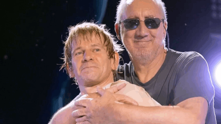 Pete Townshend hugging drummer Zak Starkey on stage during a live performance, both smiling under concert lights
