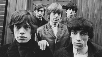 The Rolling Stones in 1960s London standing together outside a wooden door, featuring Mick Jagger, Charlie Watts, Brian Jones, Keith Richards, and Bill Wyman