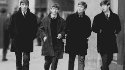 The Beatles walking together in classic black coats during their early years in London.