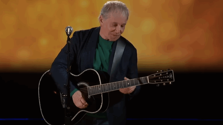 paul simon playing a black acoustic guitar