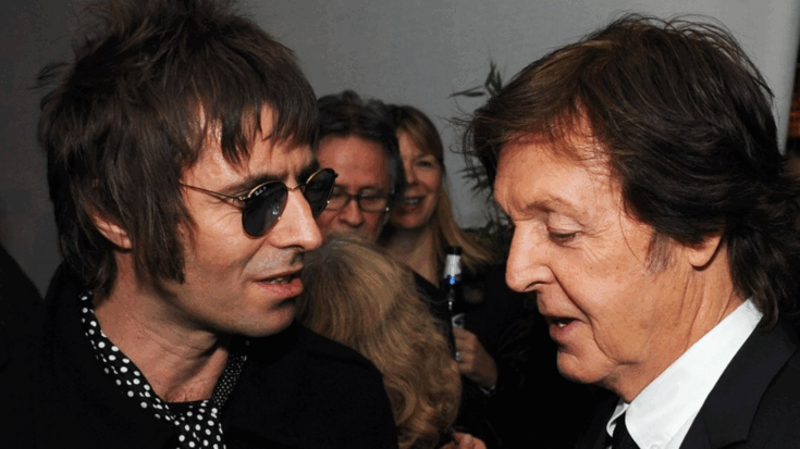 Liam Gallagher and Paul McCartney having a casual conversation at a social event, surrounded by other guests.