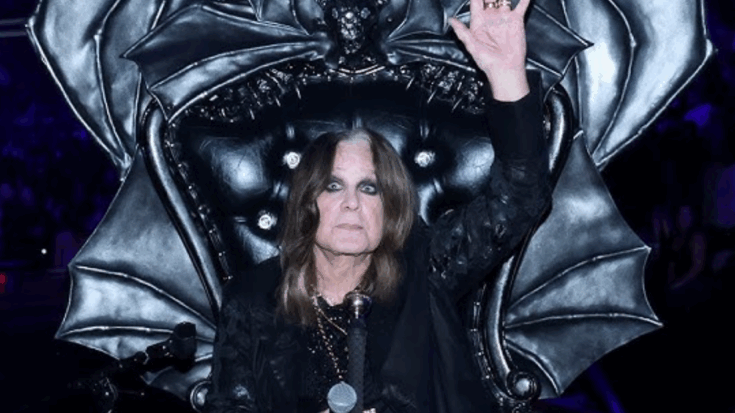 Ozzy Osbourne performing on stage seated on a gothic throne with bat wings, holding a mic and waving his hand