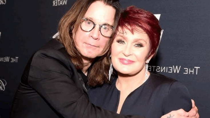 Ozzy Osbourne with long hair and glasses warmly embracing Sharon Osbourne, who has short red hair and is wearing elegant earrings, both smiling at a formal event backdrop.