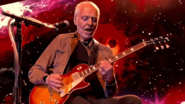 Peter Frampton playing electric guitar on stage with a cosmic galaxy-themed background