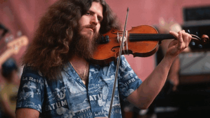 Robby Steinhardt playing violin on stage with long curly hair, thick beard, and a vibrant blue shirt during a live performance