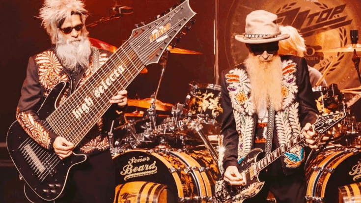 ZZ Top members performing onstage wearing embroidered jackets and sunglasses, with one playing a custom multi-string bass labeled “High Secreto” and the other playing a black electric guitar in front of custom drum kits.