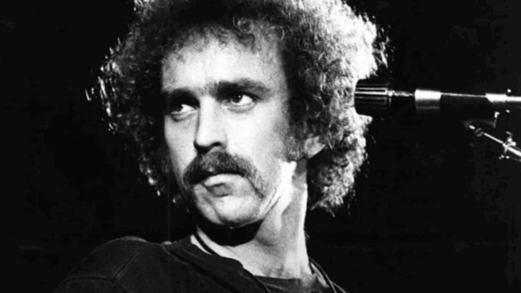 Bernie Leadon performing on stage, looking to the side, with a microphone positioned nearby.
