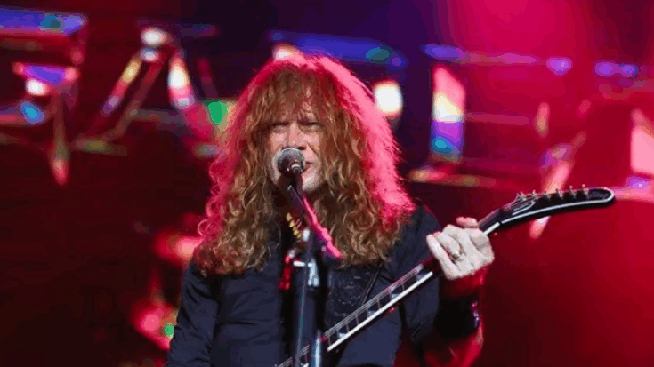 Dave Mustaine playing guitar and singing on stage under colorful lights.