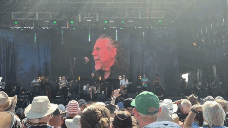 Deborah Bonham Band performing on an outdoor stage with Robert Plant singing and Dave Pegg playing, as a large crowd watches under the sun.