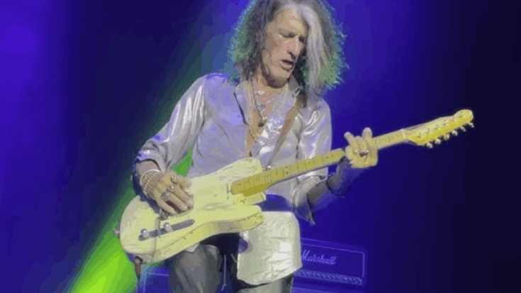 Joe Perry playing guitar on stage under bright lights