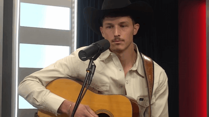 Spencer Hatcher wearing a black cowboy hat and cream-colored shirt, playing an acoustic guitar and singing into a microphone in a studio setting.