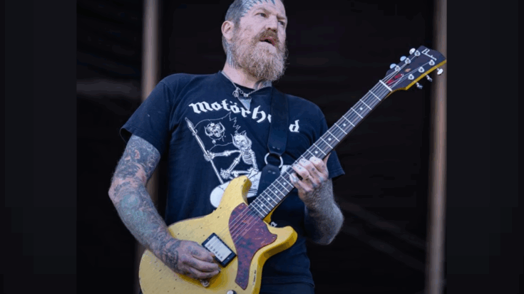 William Brent Hinds performing on stage with a yellow electric guitar, wearing a Motörhead shirt.