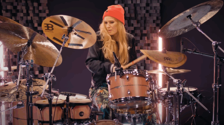 Anika Nilles performing on a pink Star Maple drum kit, wearing a red beanie and patterned pants in a studio setup.