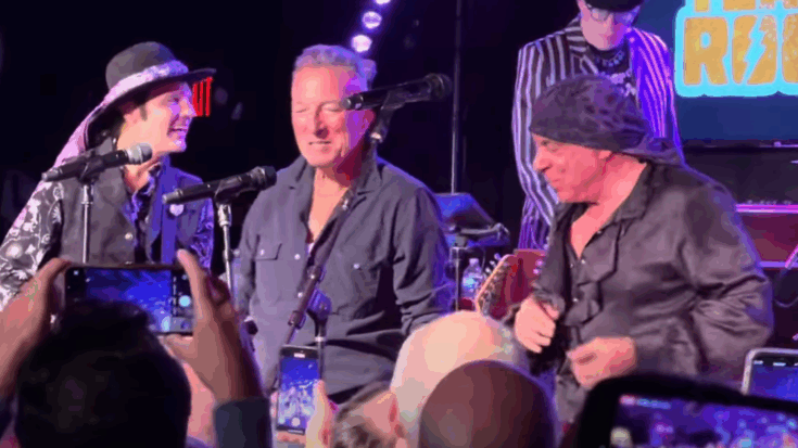 Bruce Springsteen performs alongside Little Steven and the Disciples of Soul during an energetic live rendition of “Raise Your Hand,” surrounded by fans capturing the moment.