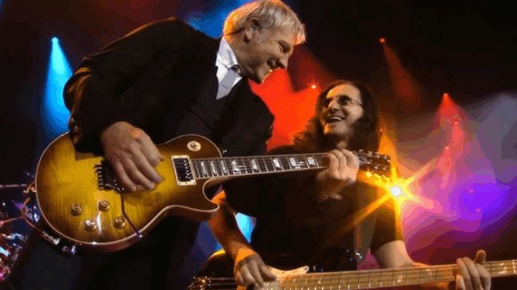 Geddy Lee and Alex Lifeson performing together on stage under colorful concert lights.