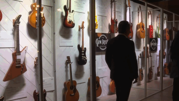 A man observes a display of vintage guitars from the Jim Irsay Collection, featuring iconic electric and acoustic instruments showcased in glass cases.