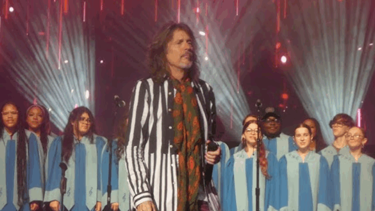 Kelly Hansen stands on stage delivering a farewell speech during Foreigner’s performance at Hard Rock Atlantic City, joined by a choir under dramatic stage lighting.