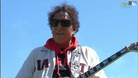 Neal Schon wearing a white jacket and sunglasses and playing his les paul guitar