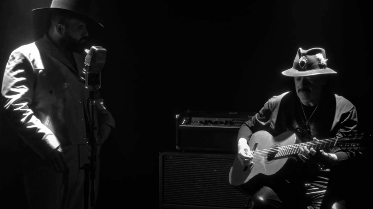 Carlos Santana performs alongside Carin Leon during the recording of their collaborative song “Velas,” blending Latin rock and modern regional sounds under moody stage lighting.