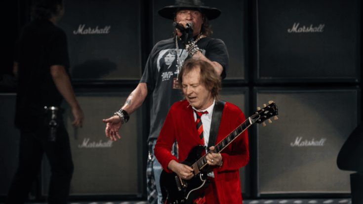 Axl Rose sings behind Angus Young as the AC/DC guitarist tears through a live performance in his signature red schoolboy outfit.