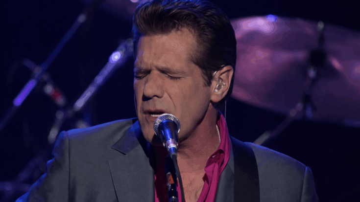 Glenn Frey sings with eyes closed into a microphone, delivering an emotional performance under blue stage lighting.