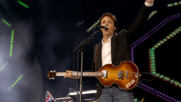 Paul McCartney sings with his Höfner bass in hand, raising one arm to fire up the crowd.