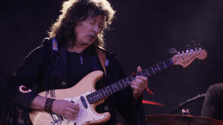 Ritchie Blackmore plays his Fender Stratocaster with intense focus under soft purple stage lights.