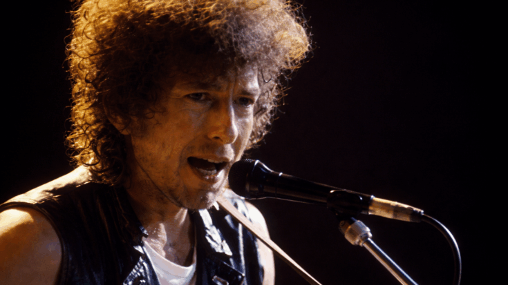 Bob Dylan sings into the microphone with intense focus, his wild curls glowing under the stage lights.