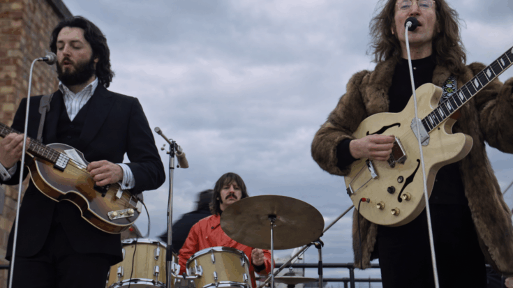 Paul McCartney sings and plays bass on a rooftop beside John Lennon on guitar, while Ringo Starr plays drums in the middle.