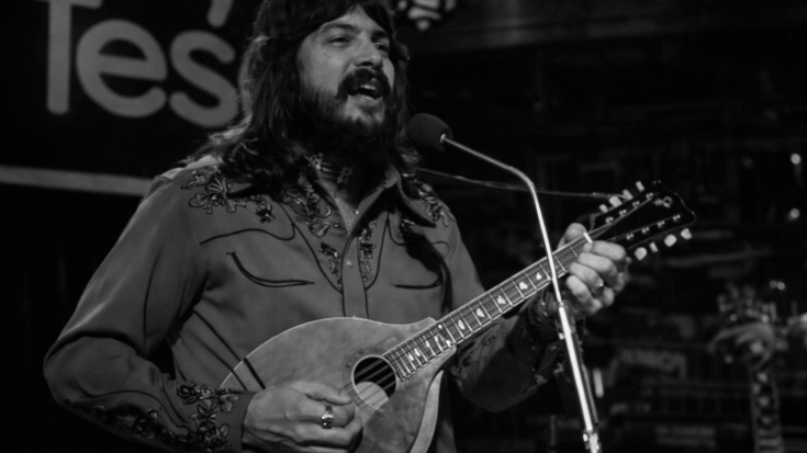 Summer Breeze' sings into a microphone while playing a mandolin in a black-and-white performance shot.