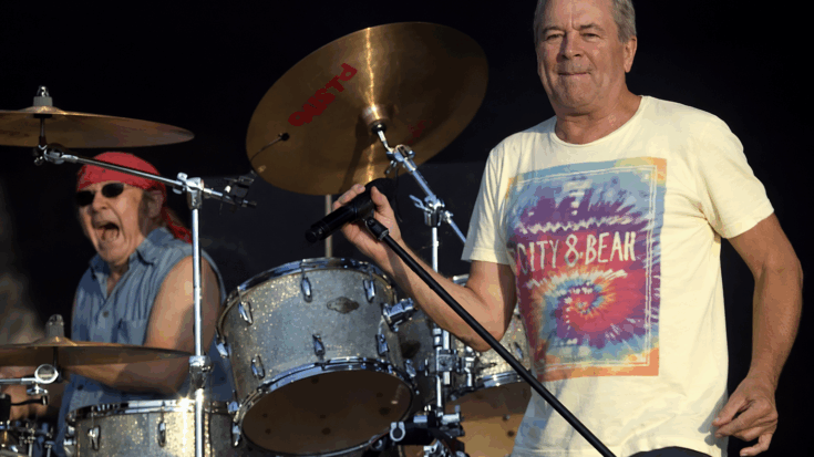 Deep Purple’s vocalist and drummer deliver an energetic live moment onstage, with the singer holding the mic while the drummer plays behind him.