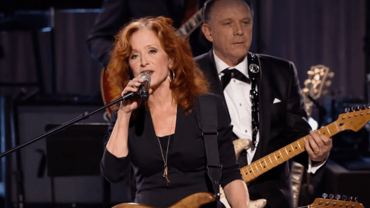 Bonnie Raitt singing into with her stratocaster.