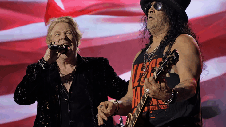 Axl Rose sings into the microphone beside Slash, who plays guitar during a high-energy Guns N’ Roses performance.