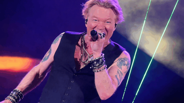 Axl Rose is caught mid-performance, singing fiercely into the microphone under bright stage lights.