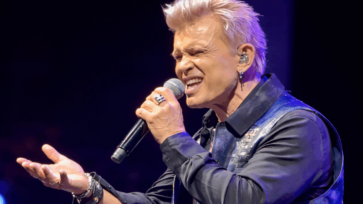 Billy Idol passionately sings into a microphone, delivering a powerful and expressive live performance.