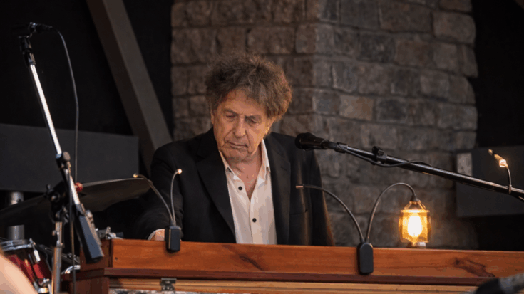 Bob Dylan stands at the keyboard with a focused look during a live performance.