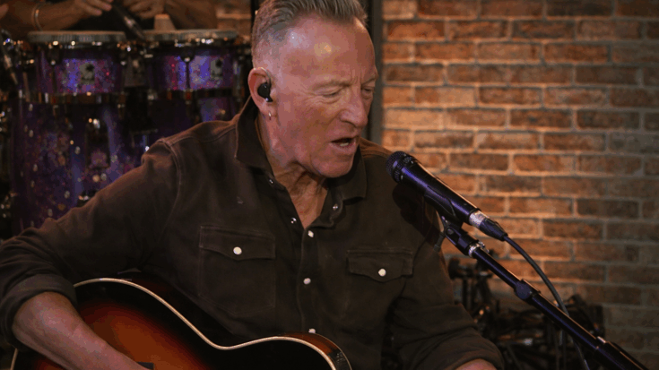 Bruce Springsteen plays an acoustic guitar and sings into a microphone during an intimate live performance.