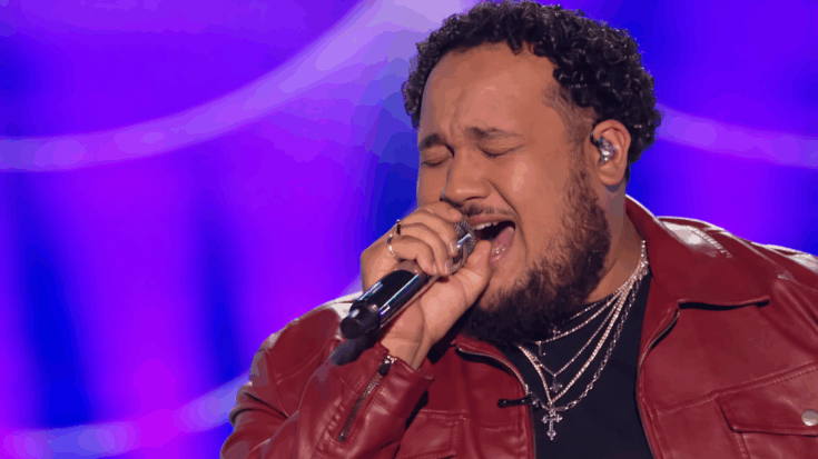 Jordan McCullough is captured mid-performance, passionately singing into a microphone under vibrant purple stage lighting.