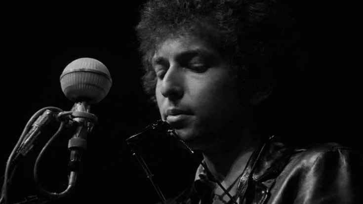 Bob Dylan appears in a moody black-and-white close-up, standing by a vintage microphone with a harmonica holder around his neck.
