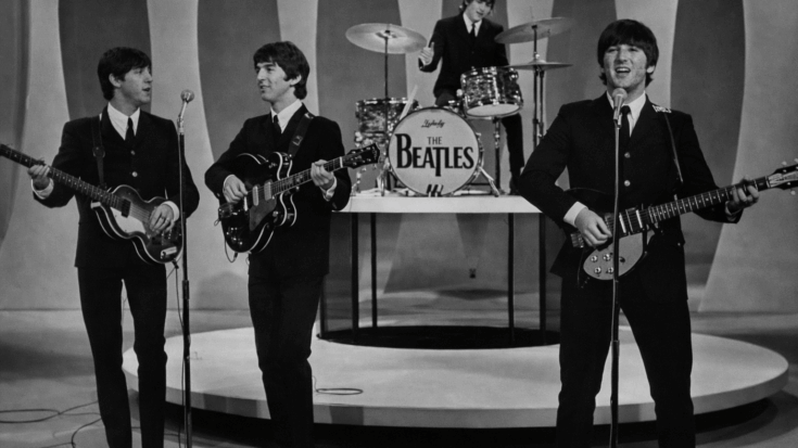 The Beatles perform together on a classic black-and-white TV stage, with their drummer playing behind them.